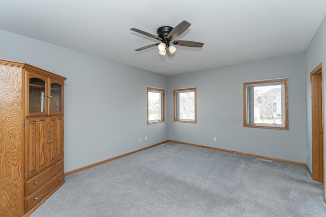 spare room featuring light colored carpet, baseboards, and ceiling fan