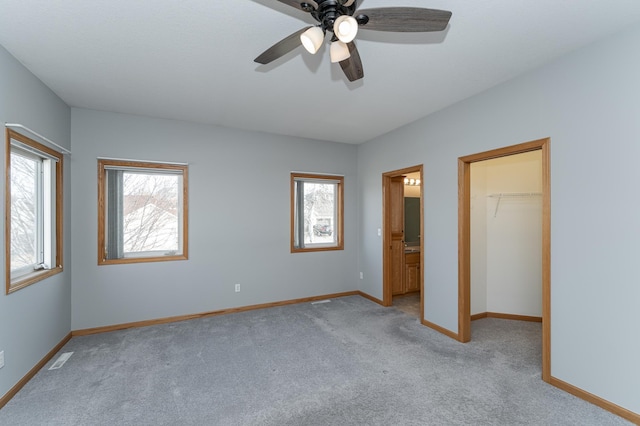 unfurnished bedroom featuring a walk in closet, multiple windows, carpet flooring, and baseboards