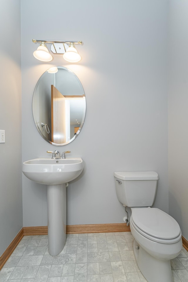 half bath featuring toilet, baseboards, and a sink