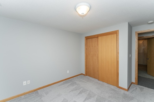 unfurnished bedroom featuring a closet, baseboards, light colored carpet, and a textured ceiling