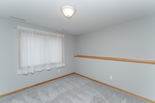 carpeted spare room with visible vents, baseboards, and a textured ceiling