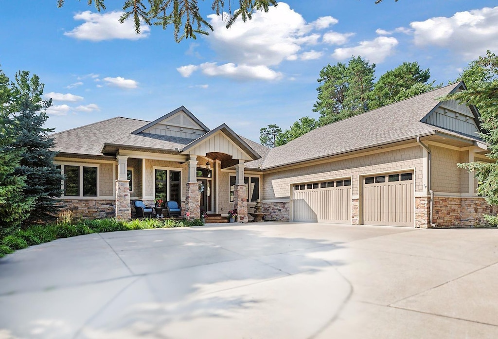 craftsman house with a garage, stone siding, roof with shingles, and driveway