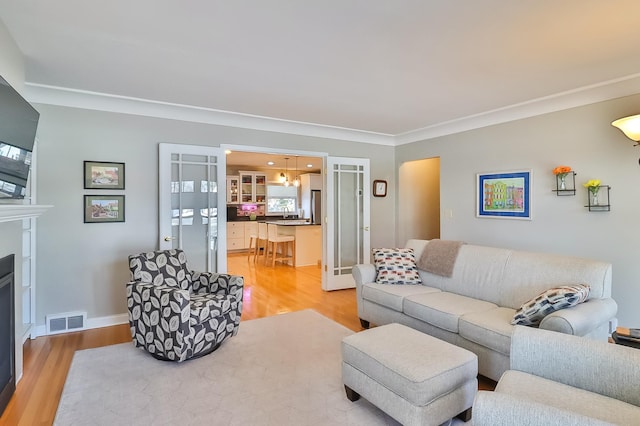 living room featuring visible vents, ornamental molding, light wood-style floors, a fireplace, and baseboards