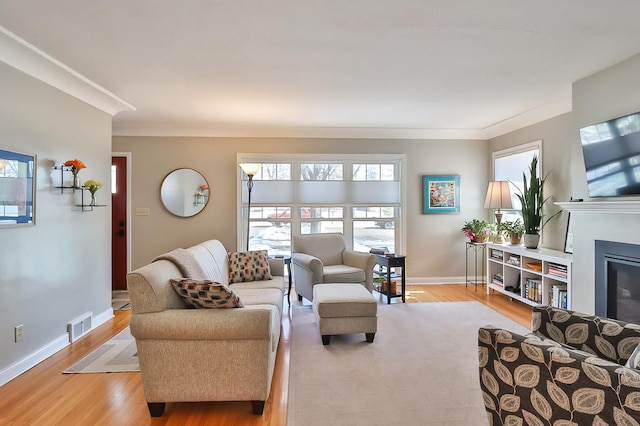 living room with visible vents, light wood-style flooring, baseboards, and a glass covered fireplace