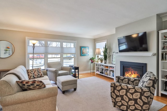 living area with a glass covered fireplace, baseboards, wood finished floors, and crown molding