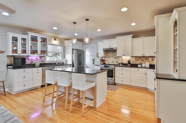 kitchen with dark countertops, a kitchen island, under cabinet range hood, and stainless steel appliances