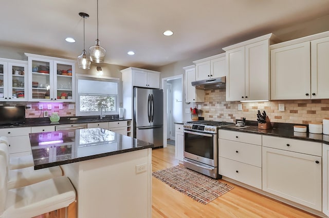 kitchen with pendant lighting, light wood-style flooring, under cabinet range hood, appliances with stainless steel finishes, and decorative backsplash