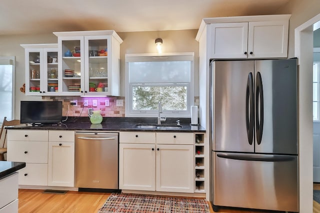 kitchen with light wood-style flooring, a sink, stainless steel appliances, glass insert cabinets, and backsplash