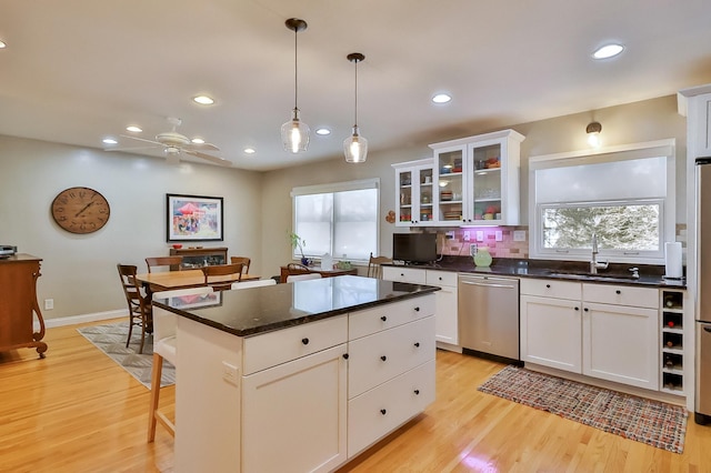 kitchen featuring a sink, decorative backsplash, white cabinets, stainless steel dishwasher, and light wood-type flooring