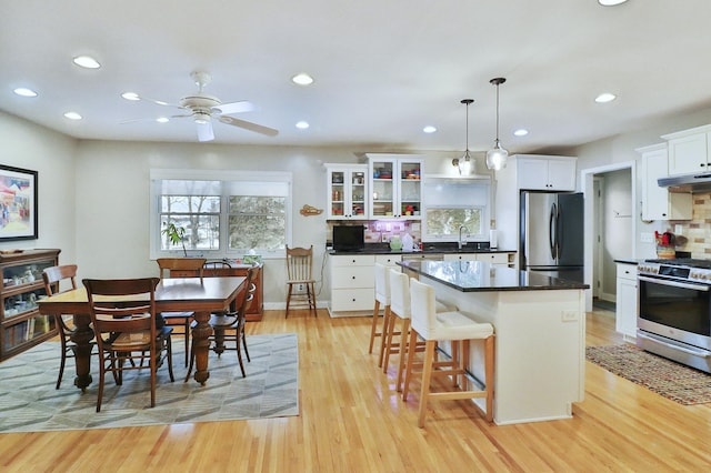 kitchen featuring under cabinet range hood, a kitchen island, backsplash, light wood-style floors, and appliances with stainless steel finishes