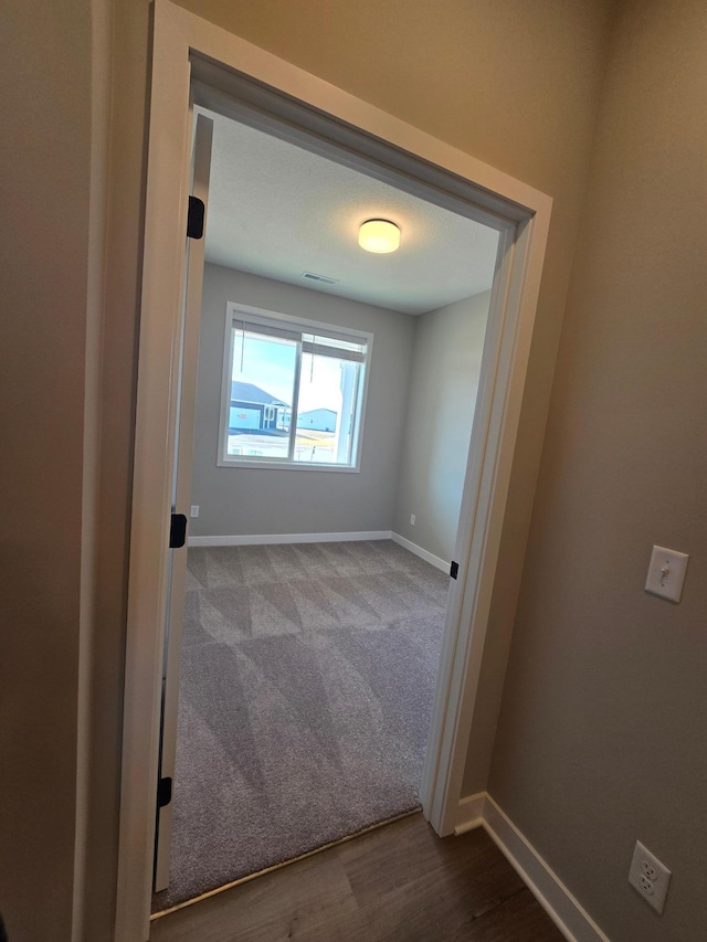 carpeted empty room featuring wood finished floors, visible vents, and baseboards