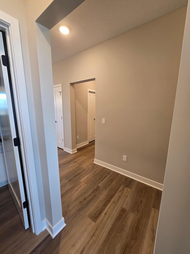 hallway featuring a textured ceiling, baseboards, and dark wood-style flooring