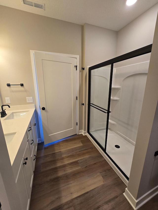 full bath with visible vents, a stall shower, a sink, a textured ceiling, and wood finished floors