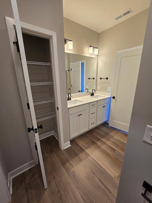 full bath featuring double vanity, visible vents, wood finished floors, and a sink