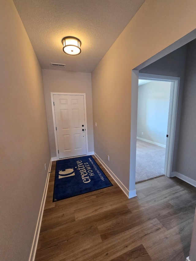 doorway with visible vents, baseboards, a textured ceiling, and wood finished floors