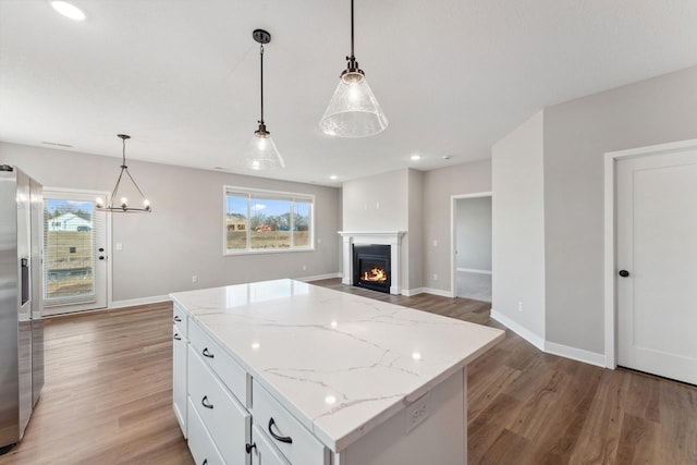1330 Rose St, New Richmond, WI 54017 - kitchen featuring light wood-style flooring, white cabinetry, a kitchen island, a chandelier, and a lit fireplace