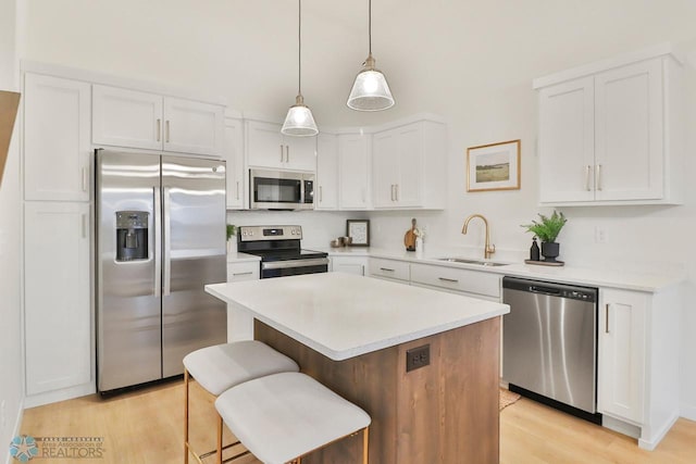 kitchen featuring a kitchen island, light wood-style flooring, stainless steel appliances, white cabinetry, and a sink