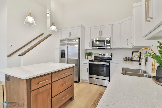 kitchen featuring light wood finished floors, a sink, stainless steel appliances, white cabinetry, and decorative light fixtures