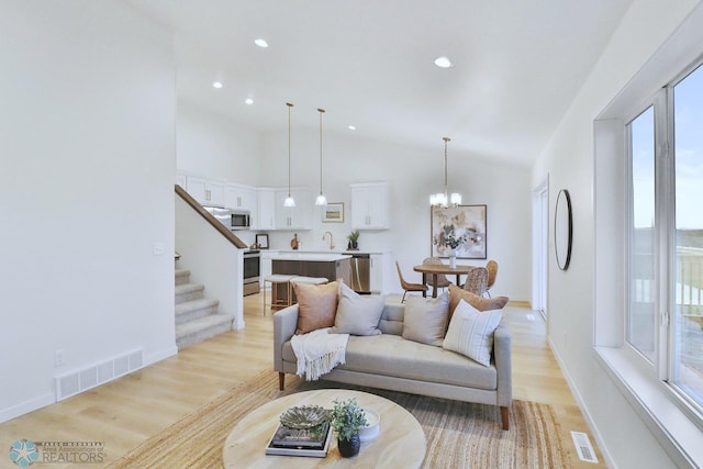 living area featuring stairway, visible vents, a chandelier, and light wood-type flooring