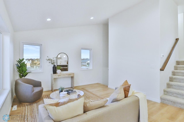 living room with stairway, plenty of natural light, light wood-style flooring, and vaulted ceiling