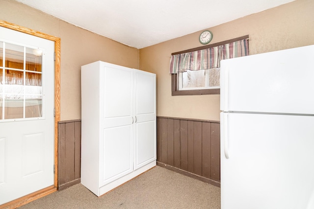 interior space featuring light carpet, a wainscoted wall, freestanding refrigerator, white cabinetry, and wooden walls