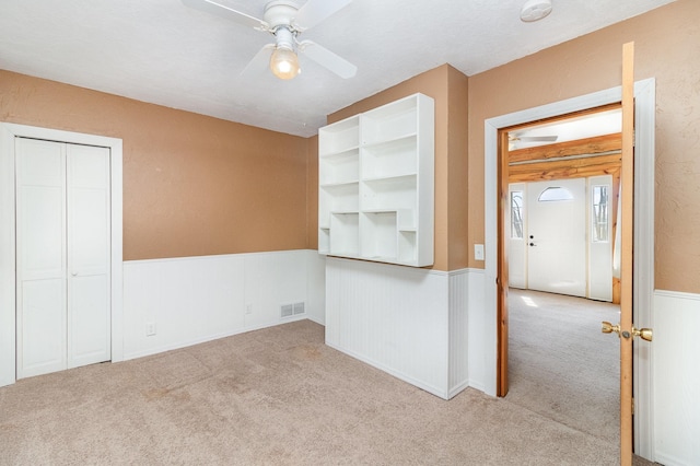 carpeted spare room featuring a wainscoted wall, visible vents, and ceiling fan