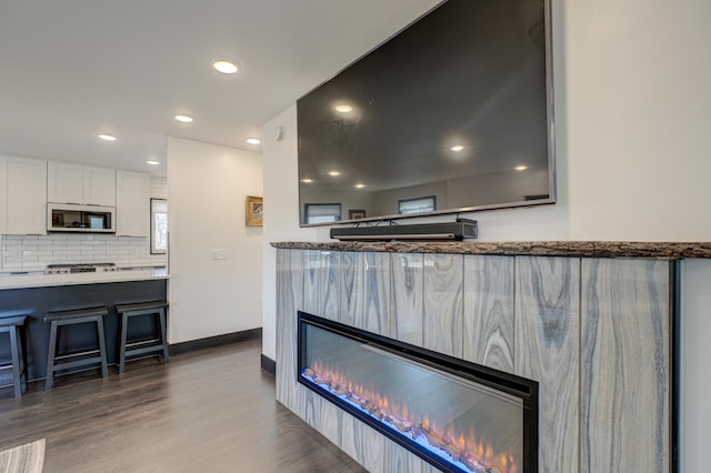1109 Saint Croix Hts, Hudson, WI 54016 - kitchen with white cabinetry, a glass covered fireplace, a kitchen bar, decorative backsplash, and wood finished floors