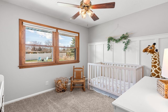bedroom with a crib, ceiling fan, carpet, and a decorative wall