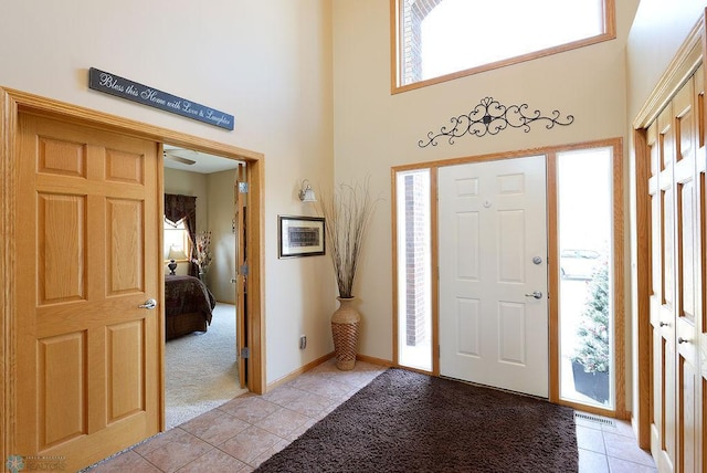 entryway featuring light tile patterned floors, light colored carpet, baseboards, and a towering ceiling