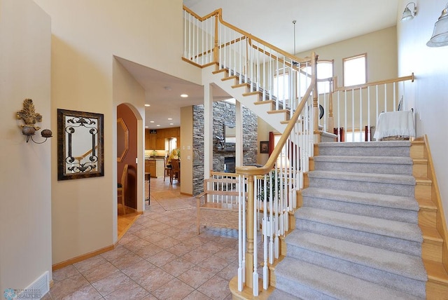 staircase with tile patterned flooring, baseboards, recessed lighting, a towering ceiling, and arched walkways