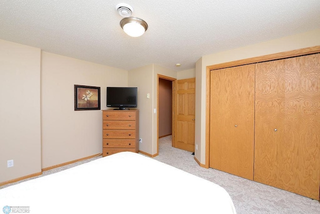 unfurnished bedroom with a closet, light colored carpet, a textured ceiling, and baseboards