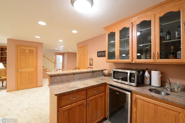 kitchen featuring stainless steel microwave, light stone countertops, wine cooler, a peninsula, and a sink