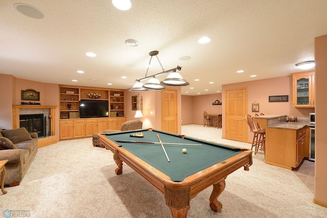 playroom with light carpet, beverage cooler, a textured ceiling, a glass covered fireplace, and recessed lighting