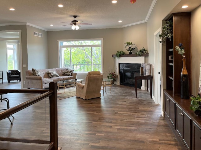 living room with visible vents, recessed lighting, dark wood-style flooring, a glass covered fireplace, and crown molding