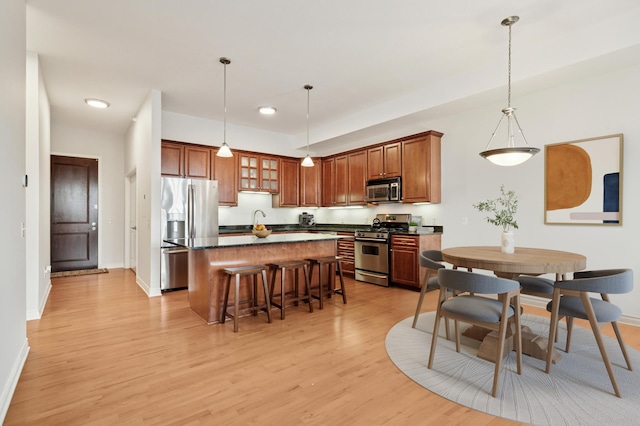 kitchen with a breakfast bar, stainless steel appliances, dark countertops, light wood-type flooring, and a center island