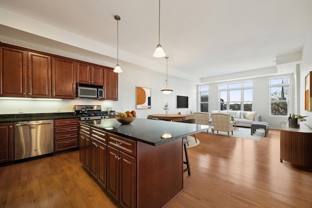 kitchen featuring dark countertops, open floor plan, a breakfast bar area, appliances with stainless steel finishes, and wood finished floors