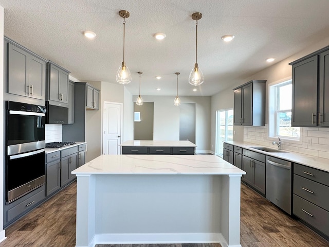 kitchen featuring dark wood-style flooring, a sink, decorative backsplash, stainless steel appliances, and a center island