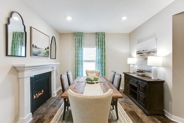 dining room featuring a glass covered fireplace, dark wood-type flooring, baseboards, and a textured ceiling