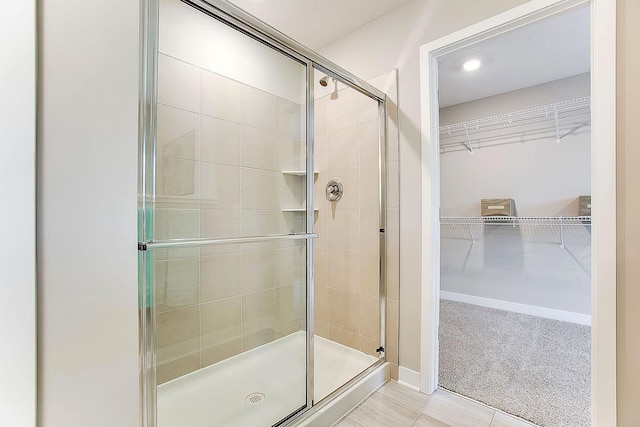 full bathroom with a stall shower, a walk in closet, and baseboards