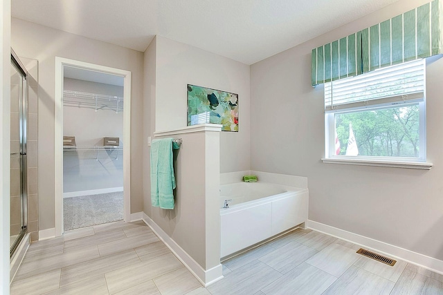 bathroom featuring baseboards, visible vents, a shower stall, a spacious closet, and a garden tub