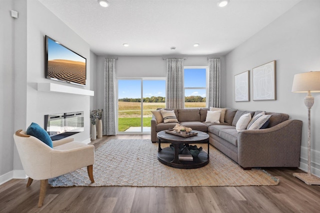 living room with a glass covered fireplace, recessed lighting, wood finished floors, and baseboards