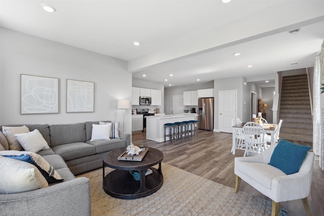 living area with recessed lighting, wood finished floors, and stairs