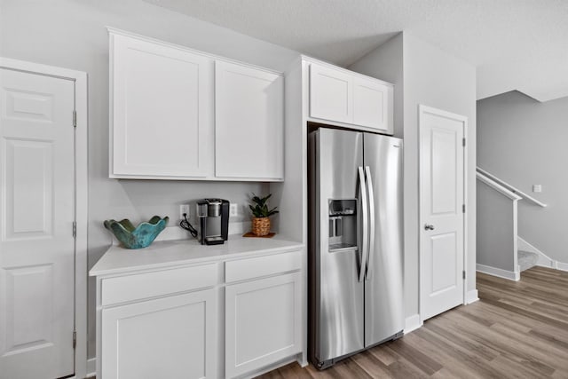 kitchen with white cabinetry, stainless steel fridge, light wood-style floors, light countertops, and baseboards