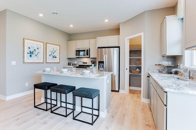 kitchen featuring a kitchen island, a sink, stainless steel appliances, a kitchen bar, and light wood-type flooring