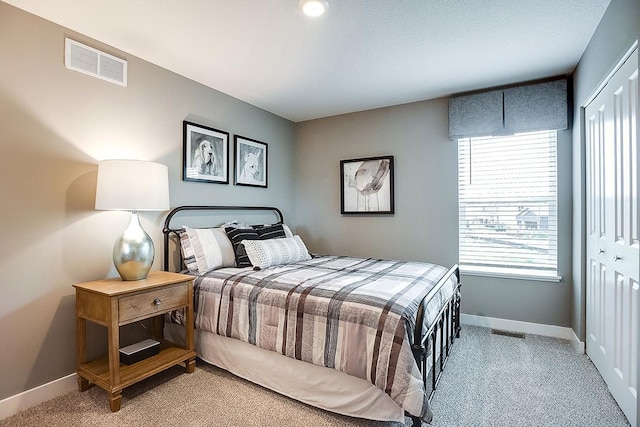 bedroom with a closet, visible vents, light carpet, and baseboards