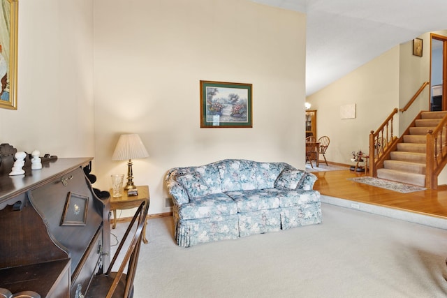 carpeted living area with baseboards, stairs, and vaulted ceiling