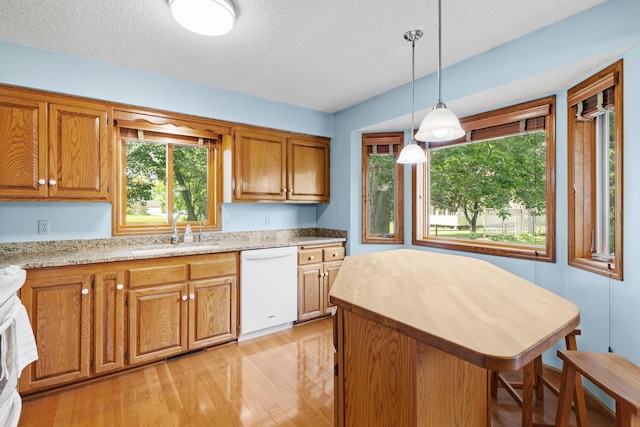 kitchen with a sink, light wood-style floors, dishwasher, decorative light fixtures, and brown cabinets