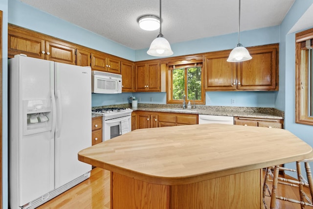 kitchen featuring light wood-type flooring, decorative light fixtures, a sink, white appliances, and brown cabinetry