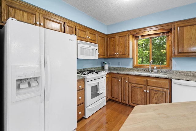 kitchen featuring white appliances, wood finished floors, brown cabinets, and a sink