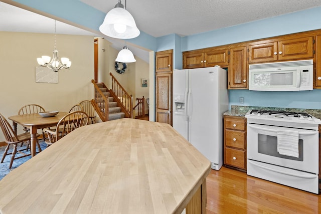 kitchen featuring pendant lighting, light wood-style floors, brown cabinetry, white appliances, and a textured ceiling